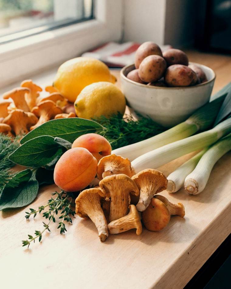 Kantareller, aprikoser, purjolök, färskpotatis, salvia och timjan på en köksbänk